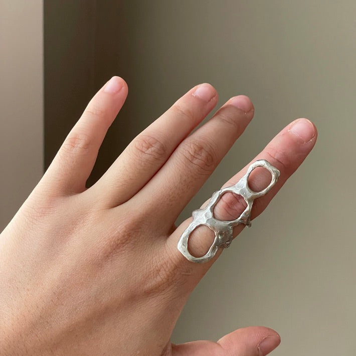 Hand wearing a silver knuckle ring against a neutral background